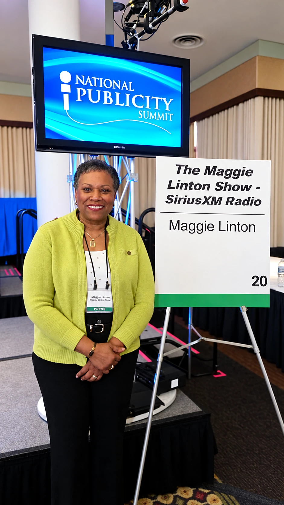 Maggie Linton at the National Publicity Summit with a sign for The Maggie Linton Show on SiriusXM Radio